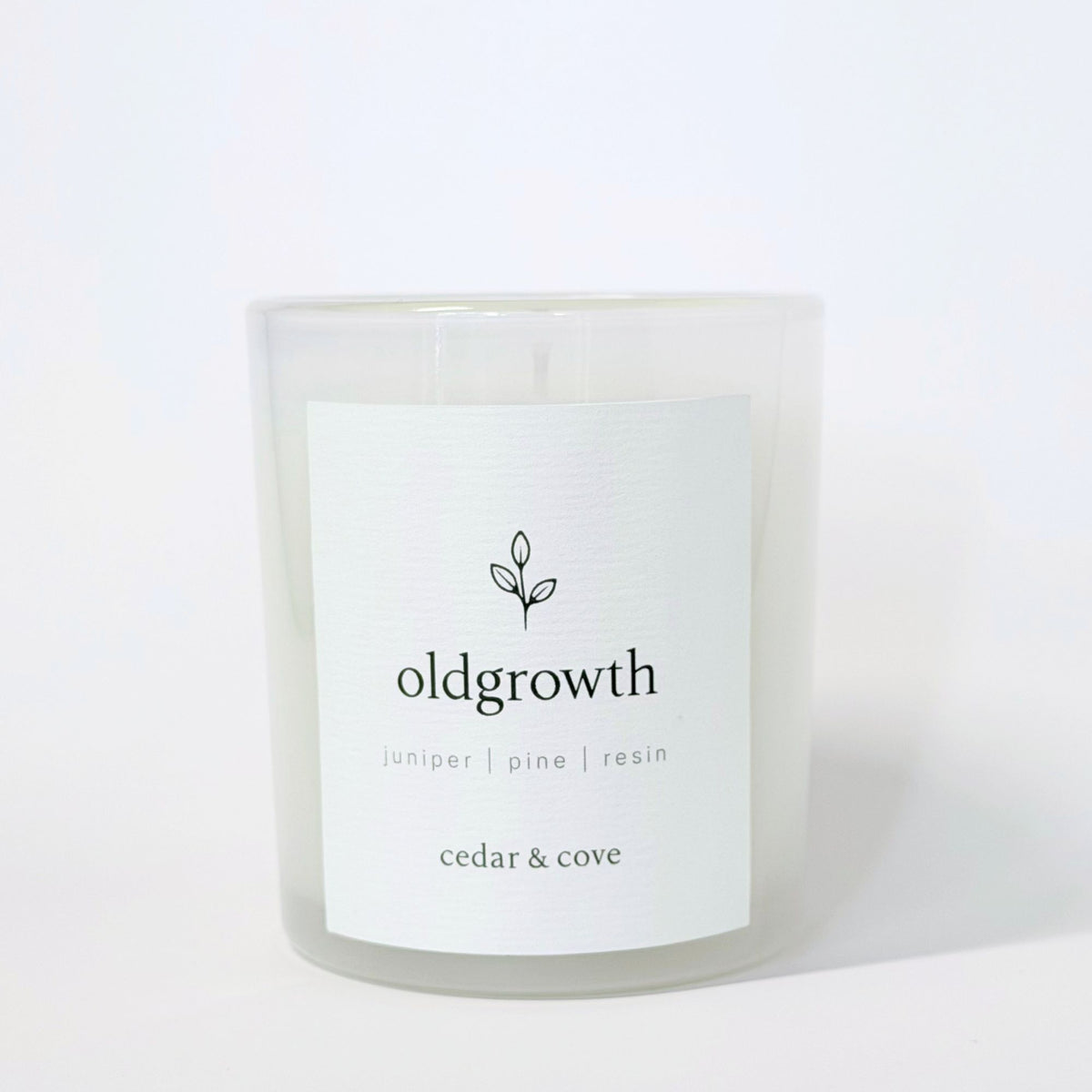 A glass jar candle called Oldgrowth by Cedar & Cove with juniper, pine, and resin scent notes. Photographed on a clean white background. 